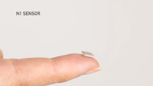 A photograph of a finger holding the Neuralink sensor., with the text "N1 Sensor".