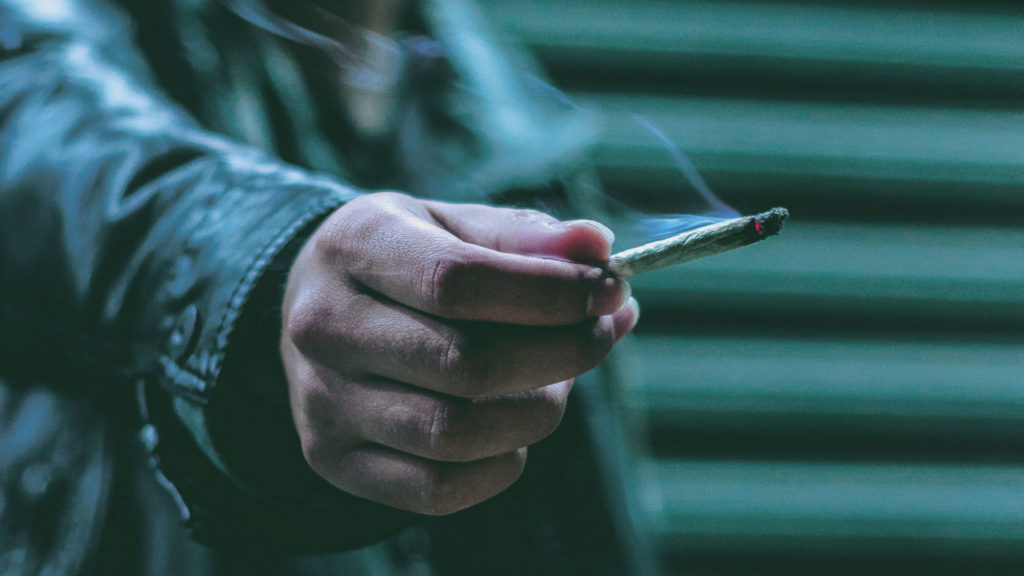 A photograph of a hand holding a lit cigarette.