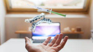 A hand catching dental equipment, with a laptop and a desk blurred out in the background.